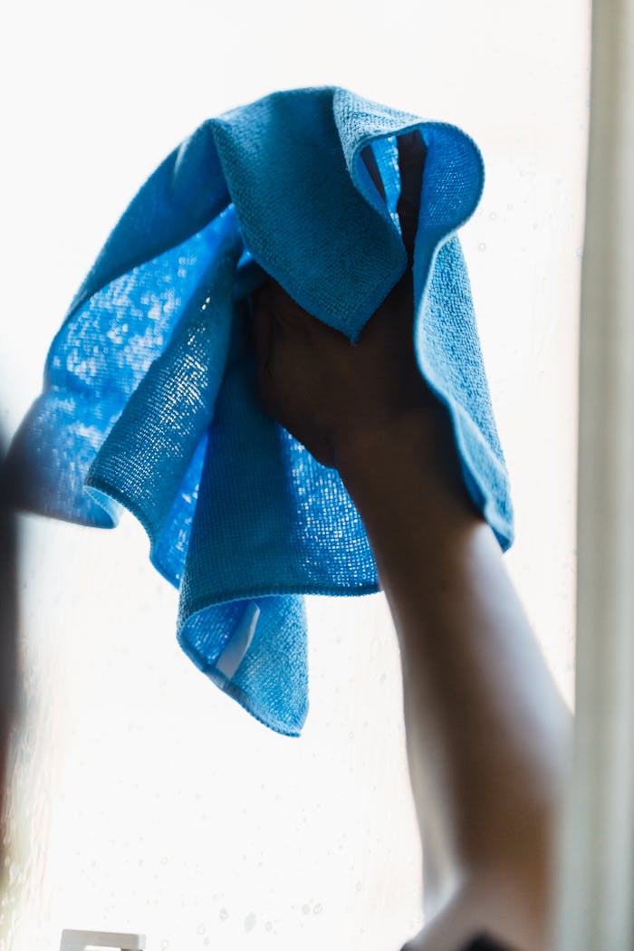 A close-up of an adult cleaning a window with a blue towel indoors. Perfect for housework and cleaning themes.