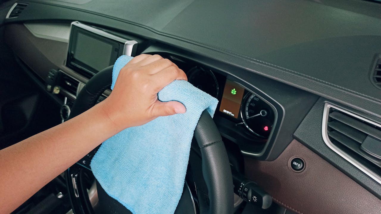 From above crop unrecognizable person polishing modern car steering wheel with blue fiber cloth
